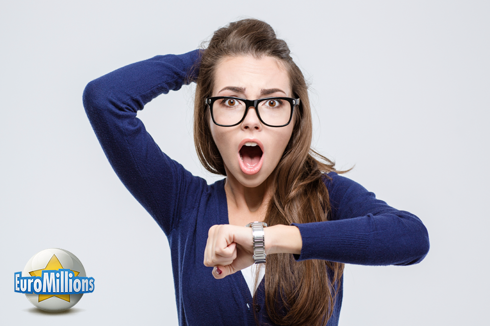 Junge Frau mit Brille schaut überrascht auf die Uhr und rauft sich die Haare