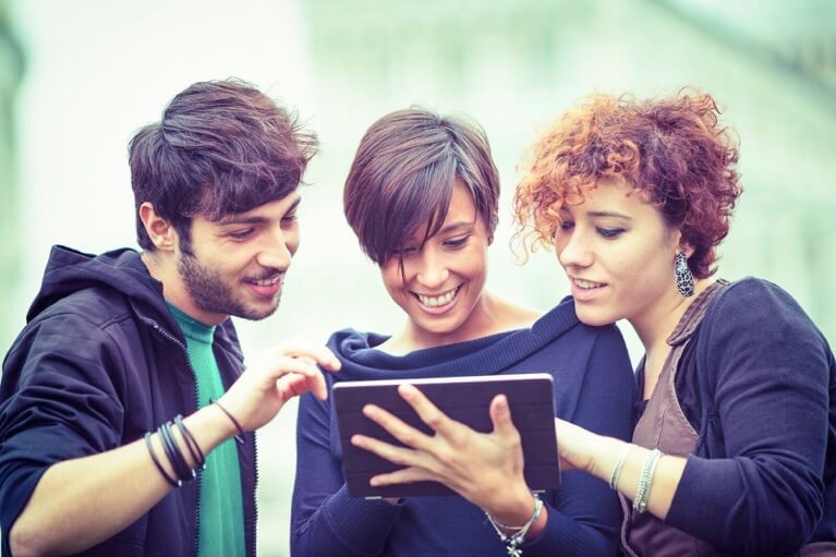 Drei junge Leute schauen lächelnd auf ein Tablet