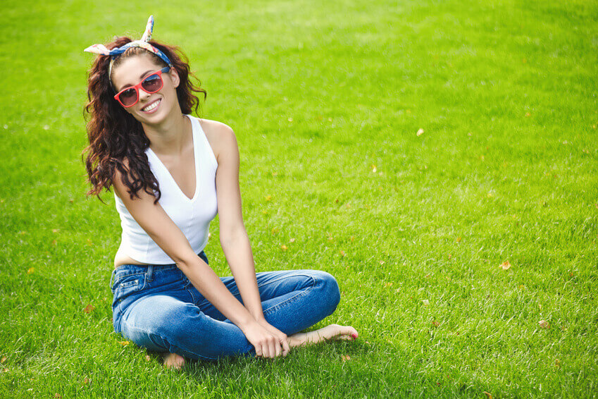 dziewczyna w okularach przeciwsłonecznych siedząca na zielonej trawie