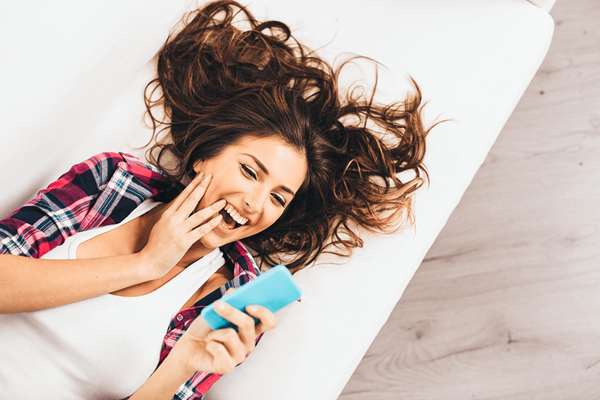 uśmiechnięta kobieta czyta jakąś dobrą wiadomość za pośrednictwem smartfona