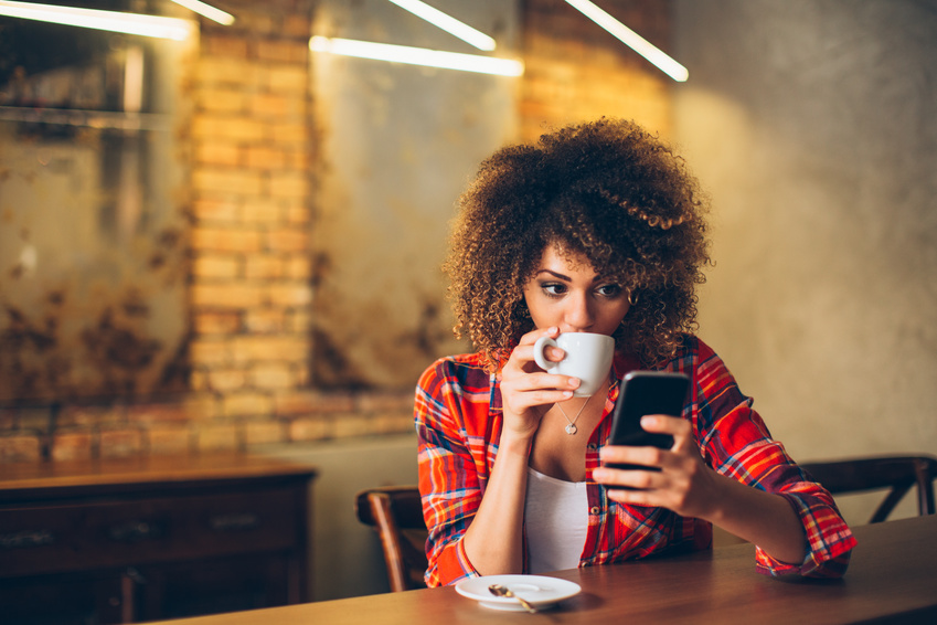 kobieta siedzi w kawiarni, gdzie pije kawę i czyta sms na swoim smartfonie